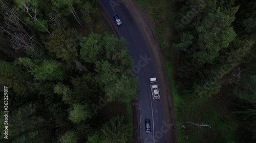 Aerial view of a large tow truck carries a broken car along a forest road.