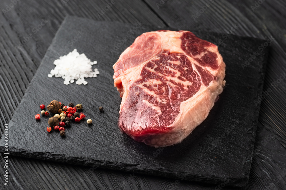Fresh raw meat with pepper on black slate, on dark background, steak Ribeye