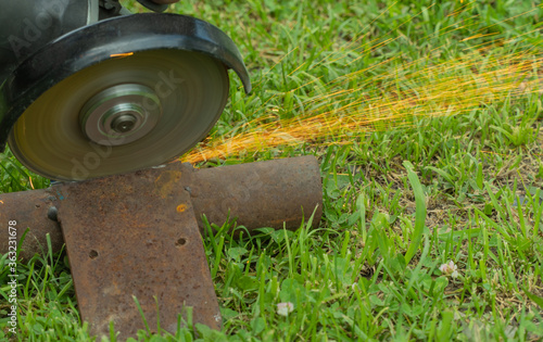 cutting metal on grass with a hand tool. sparks flying from iron. selective focus.