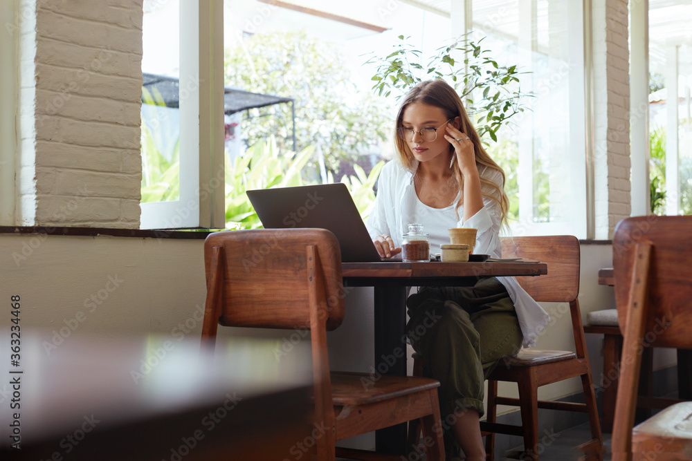 Woman. Online Work At Cafe. Beautiful Girl In Casual Clothes Working On Laptop And Touching Head. Modern Digital Technologies For Remote Job Or Education At Comfortable Workplace. Woman. Online Work At Cafe. Beautiful Girl In Casual Clothes Working On Laptop And Touching Head. Modern Digital Technologies For Remote Job Or Education At Comfortable Workplace.
