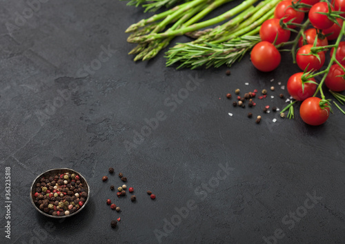 Black food background with healthy organic asparagus, cherry tomatoes and rosemary on black background with bowl of pepper.