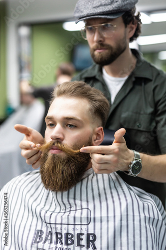 Getting perfect shape. Close-up side view of young bearded man getting beard haircut by hairdresser at barbershop