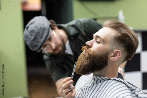 Beard styling and cut. Bearded man in barbershop corect his beard. So trendy and stylish. Advertising and barber shop concept
