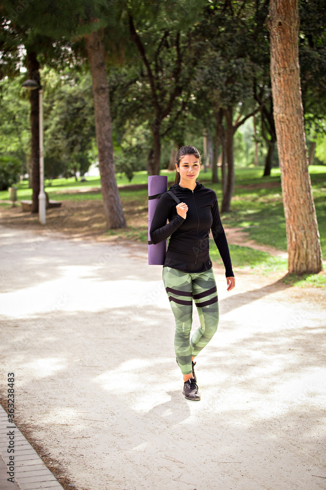 Young female walking in the park with a yoga mat over her shoulder. Young female walking in the park with a yoga mat over her shoulder.