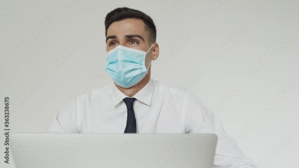 Portrait of male student with medical mask thinks during a studying on a laptop