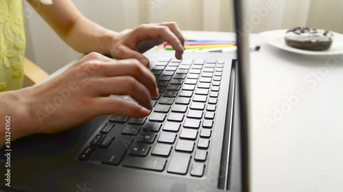 A young girl types on the laptop in the office, with sticky notes and a donut next to her. On a white table. Office scene.