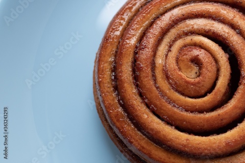 a cinnamon bun lies on a blue background. The view from the top. Sweet pastries.