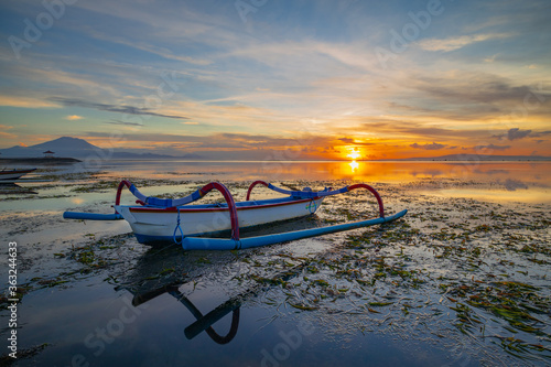 Seascape. Fisherman boat jukung. Traditional fishing boat at the beach during sunrise. Colorful sky. Amazing water reflection. Sanur beach, Bali
