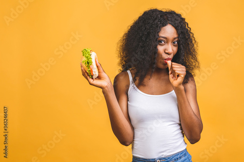 African American black beautiful young woman eating hamburger isolated on yellow background.