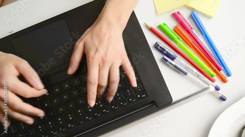 A young girl types on the laptop in the office, with sticky notes and a donut next to her. On a white table. Office overhead scene.
