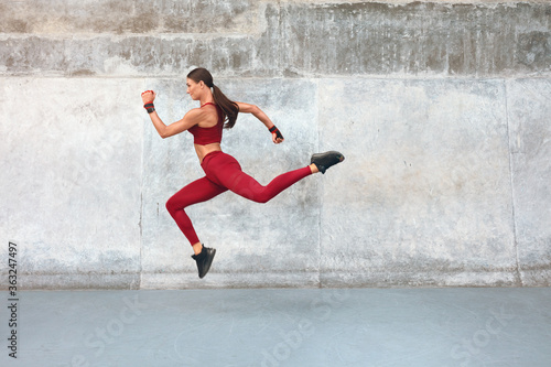 Fitness Girl Jumping. Outdoor Workout Against Concrete Wall At Stadium. Fashion Sporty Female With Strong Sexy Body In Dynamic Action Pose. Sport For Active Urban People.