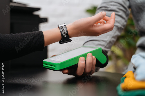 Closeup of woman paying for purchase through smartwatch using NFC technology in a clothing store. Client using watch for contactless payment in shop
