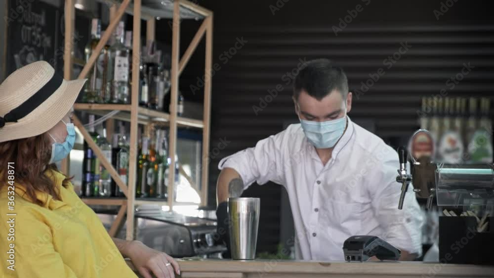 quarantine holidays, professional bartender in medical mask to protect against virus and infection prepares cocktail for visitor who takes precautions during social distancing due to pandemic and quarantine holidays, professional bartender in medical mask to protect against virus and infection prepares cocktail for visitor who takes precautions during social distancing due to pandemic and