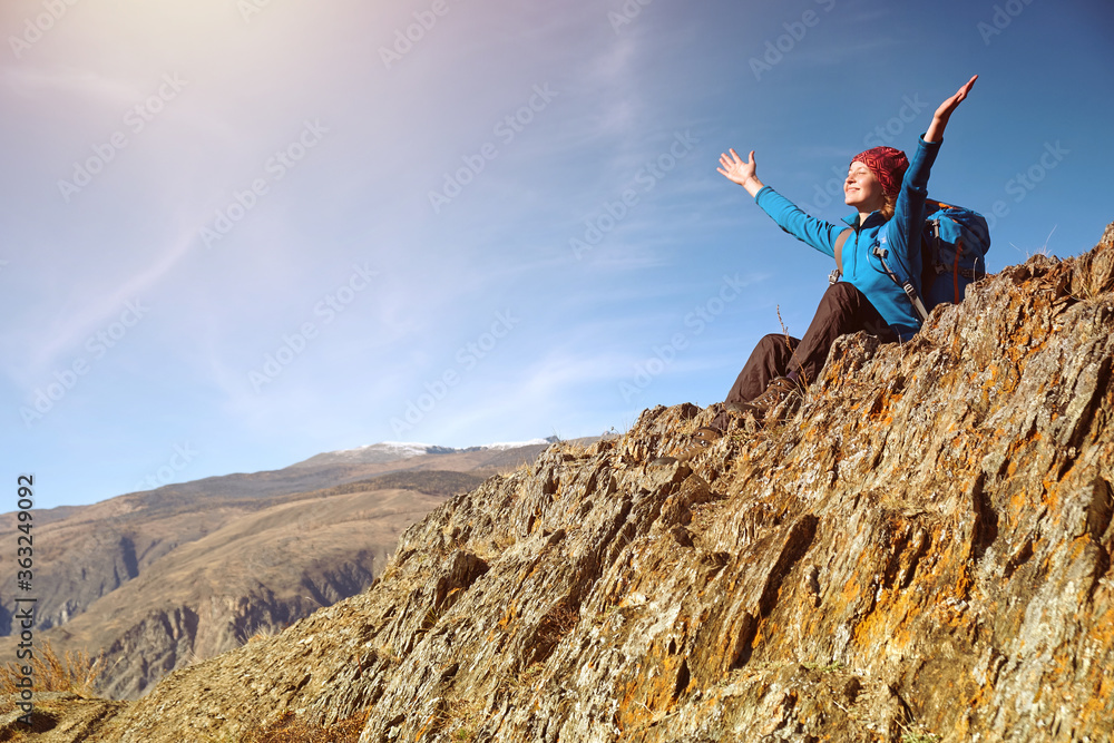 Obraz premium Hiker woman with backpack sitting on rock of a mountain and enjoying sunrise