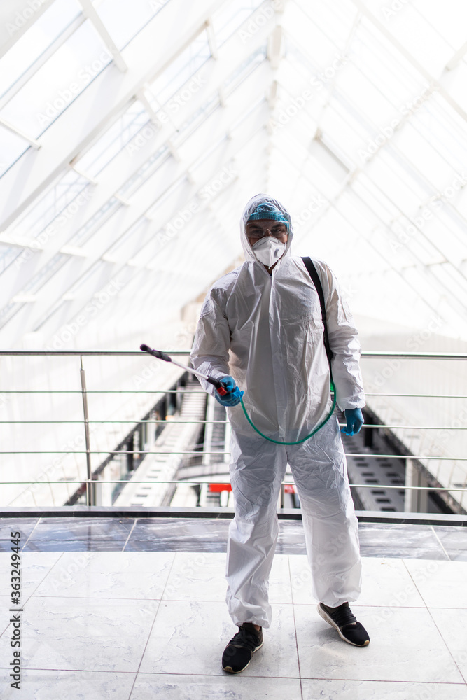 Professional fully armed disinfector against Covid-19 corona virus using sprays to remove bacteria from the surface at the hotel. Man wearing a protective mask, gloves and suit.