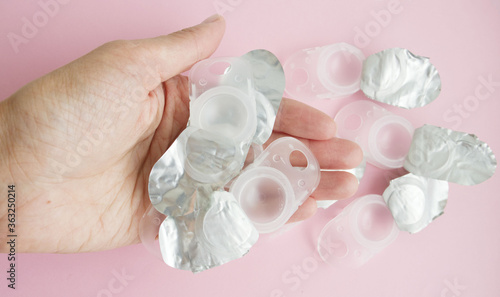 plastic, used containers, from under contact lenses, lie on the palm of a young girl, on a pink background. Vision problems, an alternative to glasses, eye comfort, increased cost of contact lenses