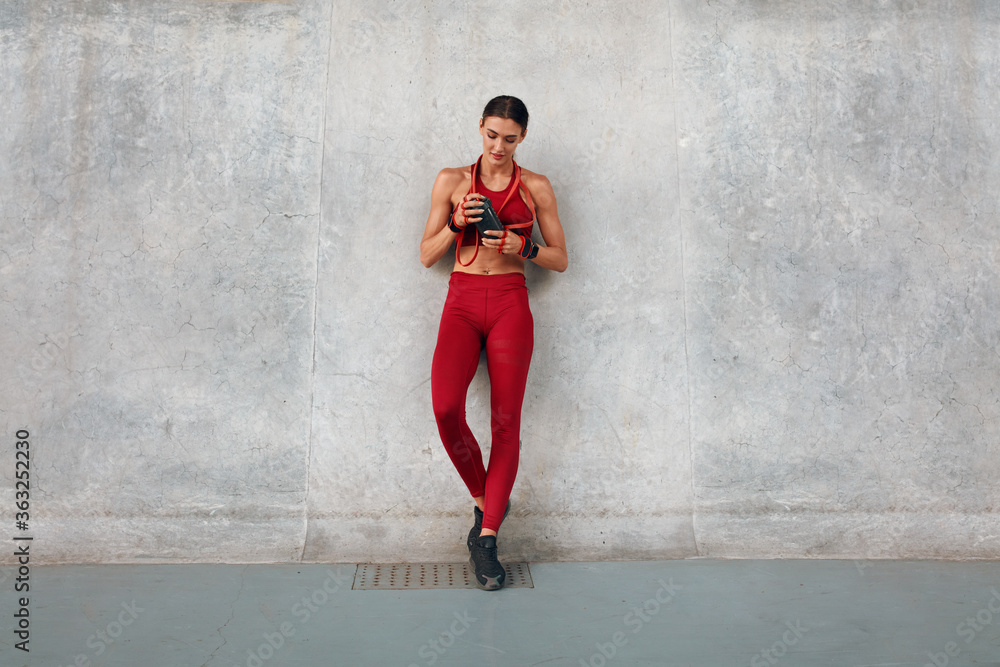 Gym. Fitness Girl With Bottle Of Protein Shake And Resistance Band Standing  Near Wall. Sporty Woman In Fashion Sportswear Between Intense Cardio  Workout. Outdoor Exercising As Urban Lifestyle. foto de Stock