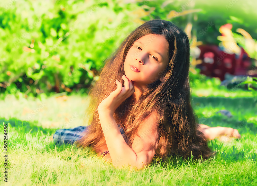 Little girl brunette in a swimsuit laying down on the green grass Little girl brunette in a swimsuit laying down on the green grass