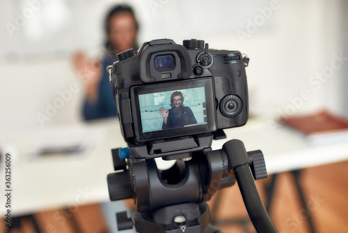 Hello. Young happy male teacher looking at camera and waving while giving online class through webcam at home. Tutor recording video tutorial. Focus on a camera screen