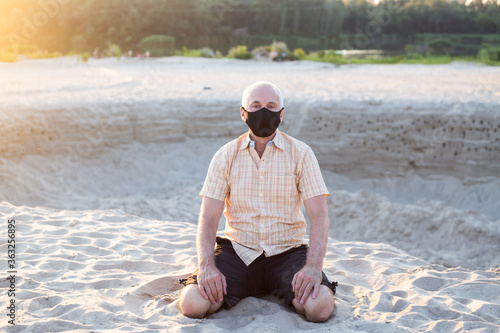 Concept of coronavirus quarantine. Senior man with medical face mask sitting in summer beach