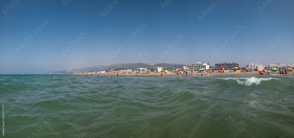 Holiday scene. View from the sea water and a wave at a travel destination with a beach at the horizon.