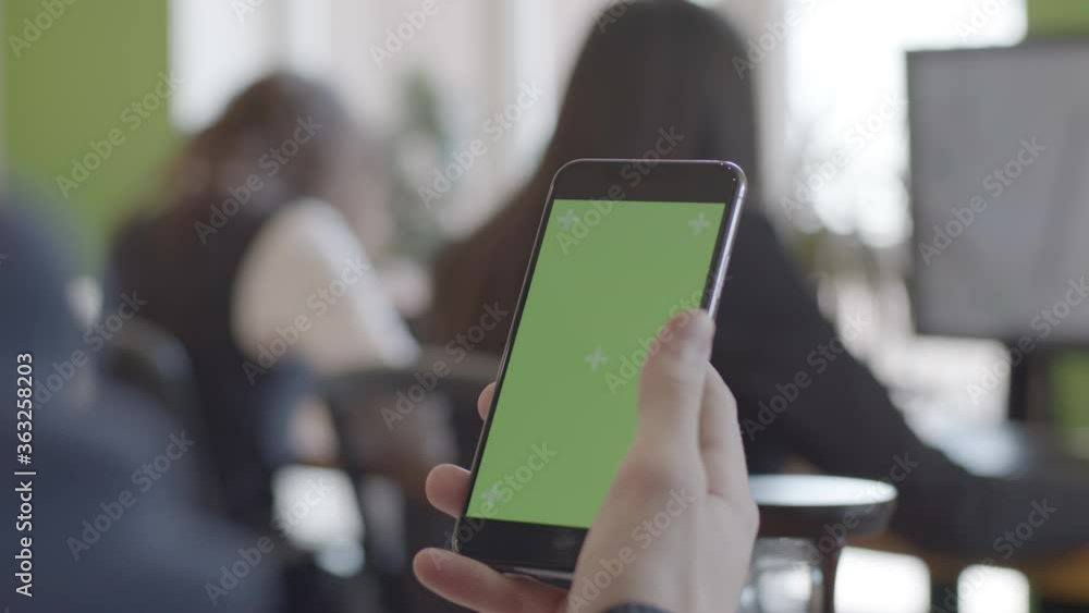 Close-up of male fingers scrolling a phone with chroma key screen in modern office on the background of employees. Close-up of male fingers scrolling a phone with chroma key screen in modern office on the background of employees.