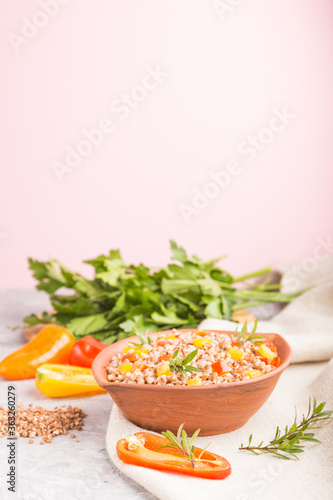 Buckwheat porridge with vegetables in clay bowl on a gray and pink background and linen textile. Side view, copy space, selective focus.