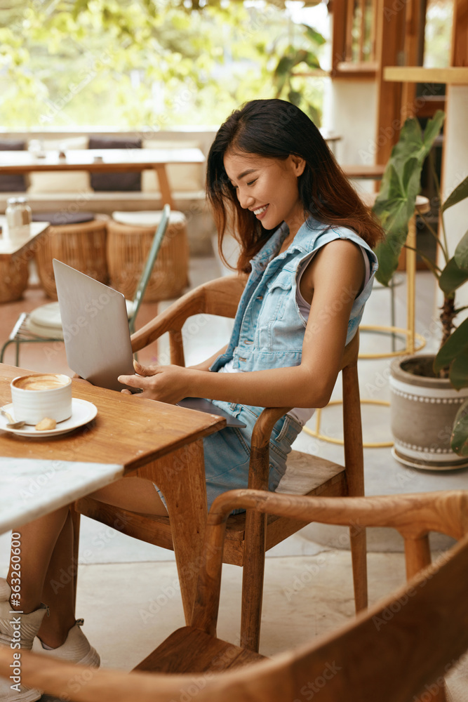 Girl At Coffee Shop. Woman Having Call On Laptop At Cafe. Beautiful Asian Model In Casual Clothes Chatting At Comfortable Workplace On Summer Vacation. Modern Technologies For Digital Nomad Lifestyle.