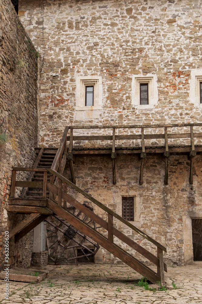 A wooden staircase in the courtyard of a stone medieval castle.