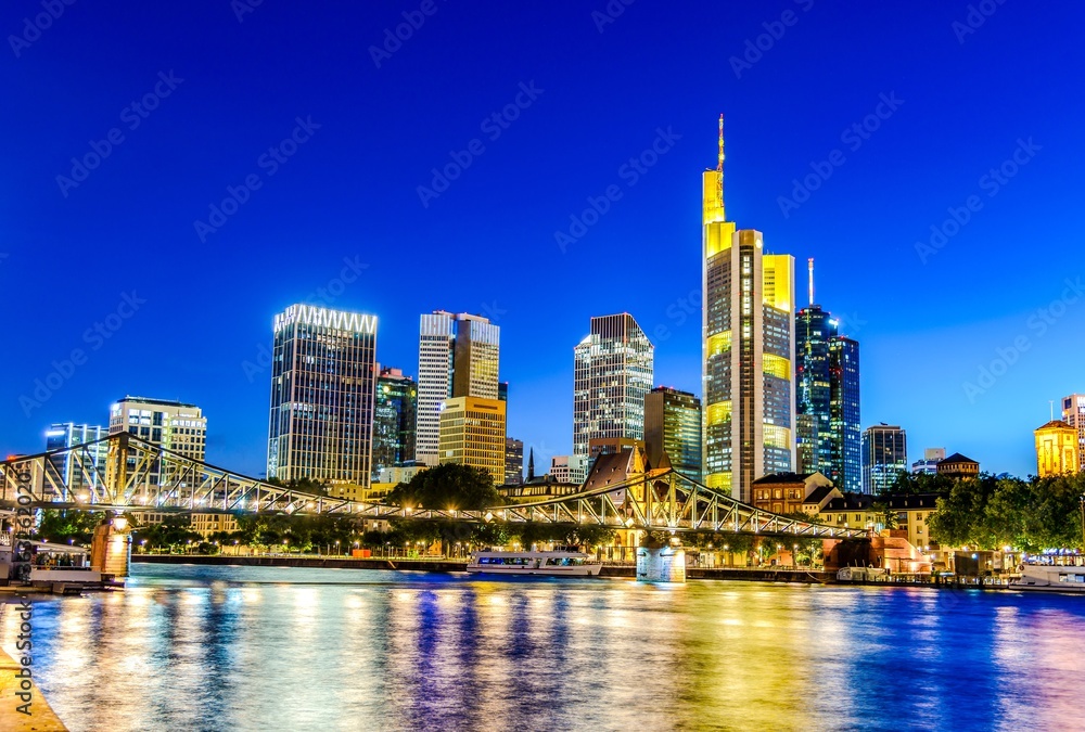 Frankfurt am Main. Skyline cityscape of European finance center city. Bridge, river during twilight blue hour, sunset at evening, night. Gold yellow color. Travel in Hesse, Germany.