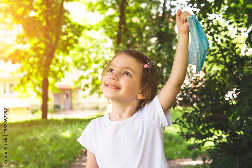 Little cute girl take off medical face mask with happy smile in the outdoor, close up. Concept of happy end and victory over coronavirus. Little cute girl take off medical face mask with happy smile in the outdoor, close up. Concept of happy end and victory over coronavirus.