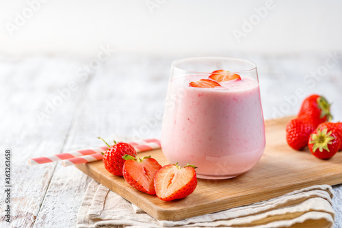 Glass with strawberry smoothie or milkshake on wooden table. Summer drink.