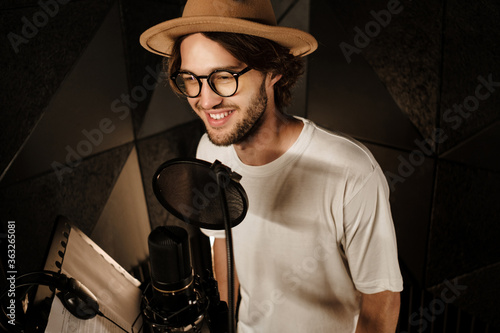 Handsome smiling male singer happily recording new song for music album in modern studio photo