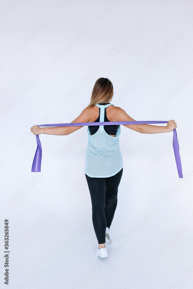 Beautiful athletic girl doing an exercise with tape . 