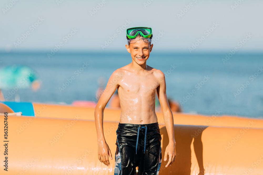 Small smiling child boy in swimming glasses, on the sea sand of the beach. Summer holiday