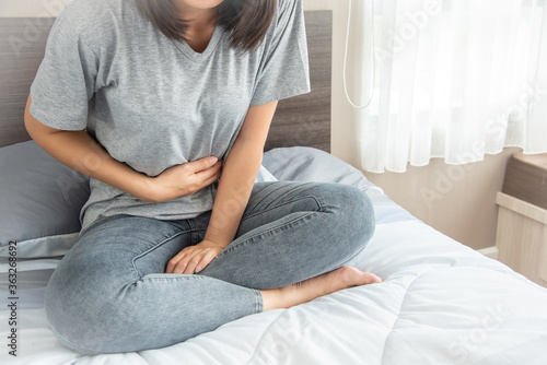 woman with stomach ache, menstrual period cramp, abdominal pain, food poisoning on bed at home