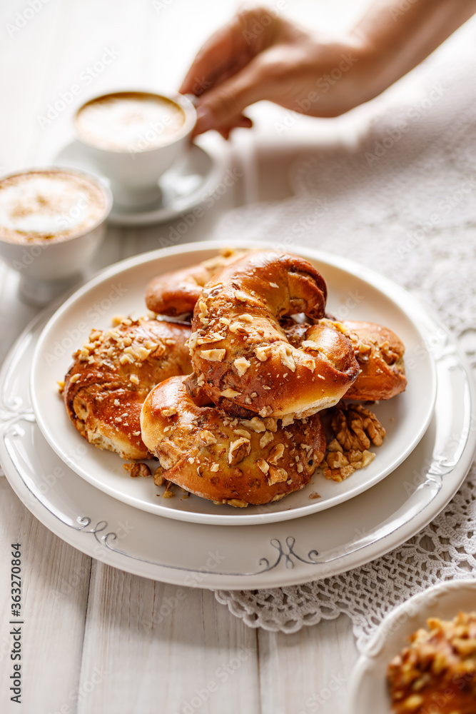 Homemade yeast croissants with cinnamon and walnuts on a plate on a wooden white table close up view Homemade yeast croissants with cinnamon and walnuts on a plate on a wooden white table close up view