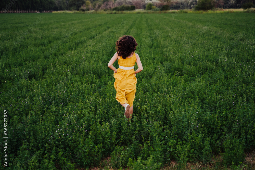portrait of young beautiful woman wearing a yellow dress running in a green field. Summertime and lifestyle portrait of young beautiful woman wearing a yellow dress running in a green field. Summertime and lifestyle