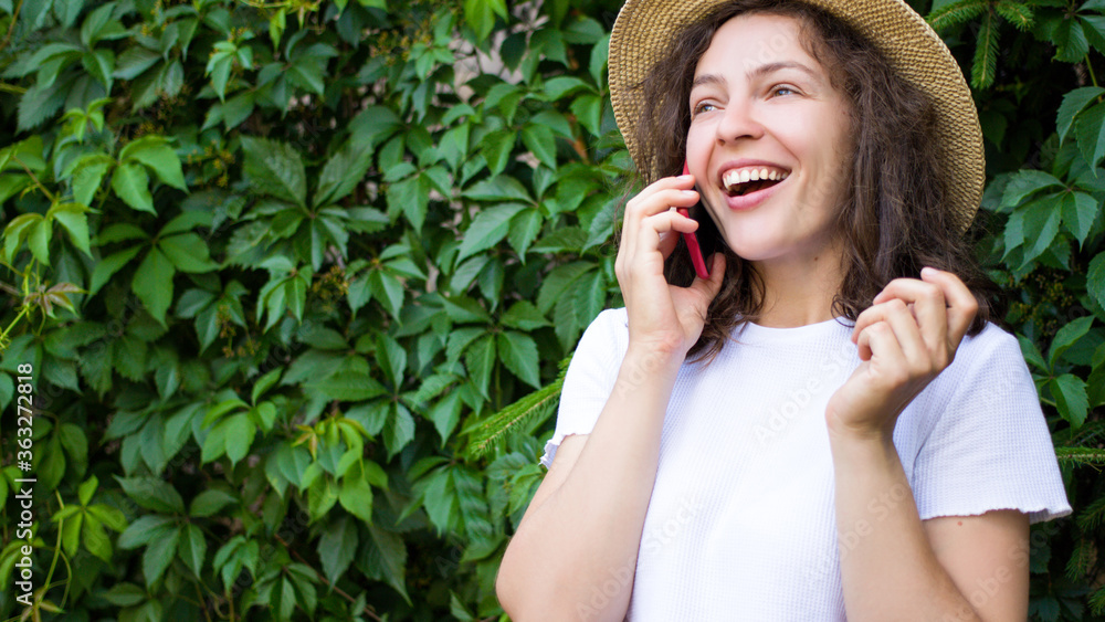 Close up excited pretty young woman talking on mobile phone,looking into the distance with happy facial expression.Cheerful girl in summer hat and white t-shirt having pleasant conversation,good news Close up excited pretty young woman talking on mobile phone,looking into the distance with happy facial expression.Cheerful girl in summer hat and white t-shirt having pleasant conversation,good news