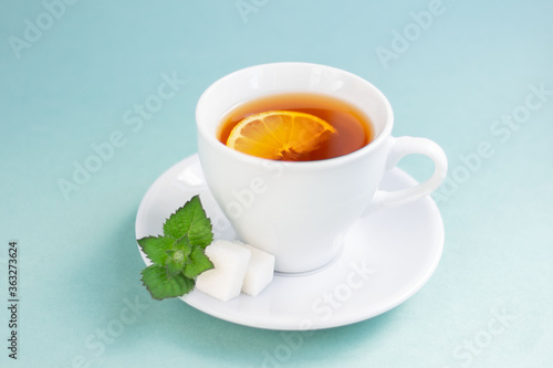A Cup of hot black tea with lemon, sugar and mint. Isolated on a light blue background. Morning composition