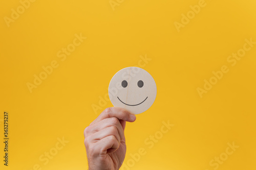 Male hand showing a wooden cut circle with smiling face on it