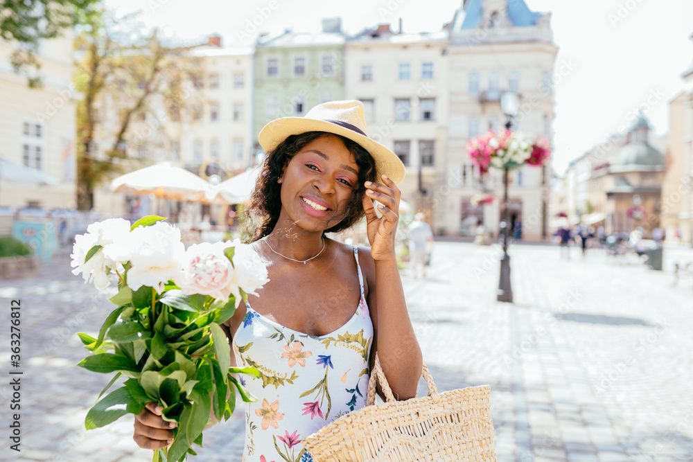 Portrait of black woman standing on the square on sunny summer or spring day outside, cute smiling african woman looking at you, attractive nigerian girl enjoying summer, filtered image.