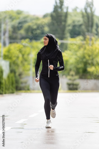 young muslim sportswoman in hijab and sportswear jogging outside