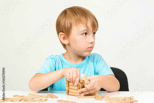 Little boy playing with building blocks on a table. Kid building wooden house.