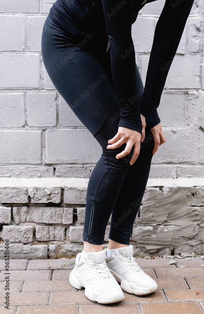 cropped view of sportswoman touching knees while exercising near brick wall
