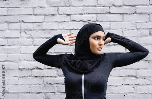 attractive muslim woman looking away while exercising near brick wall