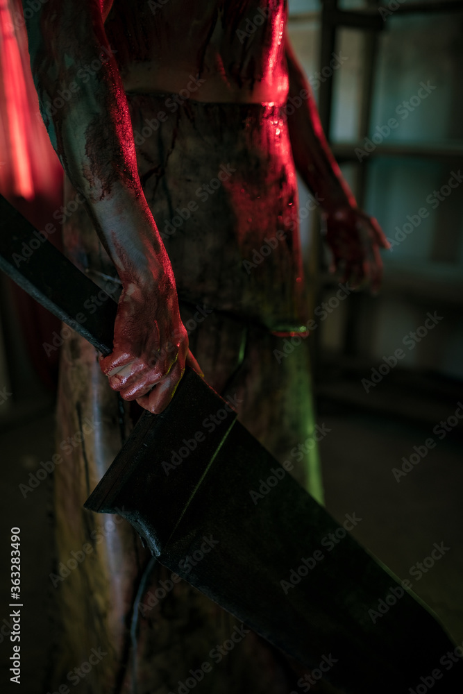 Cosplayer in the image of executioner stands in dark room with knife in his hand.