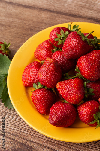 Fresh strawberries in plate on wooden table. Fresh nice strawberries. Strawberry field on fruit farm. Heap of Red strewberry on plate close up. Juice strawberry. Strawberry field on fruit farm.