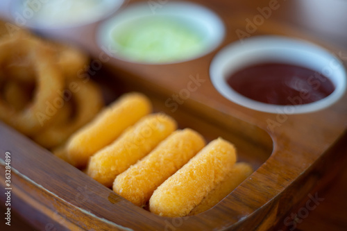 Fried cheese stick onion with sause in wooden tray.