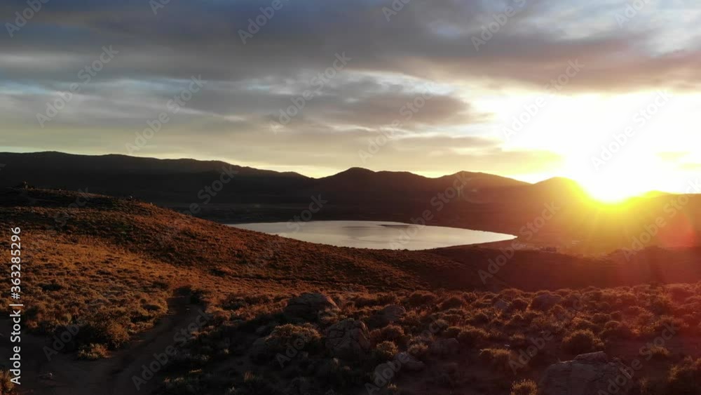Pan right reveal of sunset and sun flares over the desert with lake in valley Pan right reveal of sunset and sun flares over the desert with lake in valley